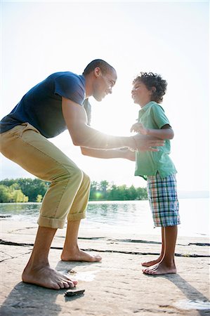 A man lifting a small boy up, playing in the sun by a lake. Photographie de stock - Premium Libres de Droits, Code: 6118-07781787