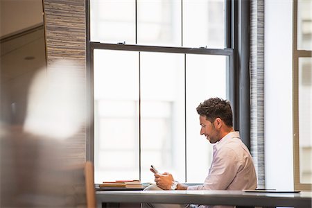 Office life. A man in an office checking his smart phone. Stock Photo - Premium Royalty-Free, Code: 6118-07781713