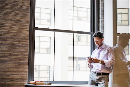 Office life. A man in an office checking his smart phone. Stock Photo - Premium Royalty-Free, Code: 6118-07781714