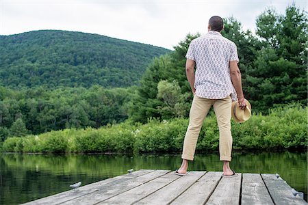 A man standing on a wooden pier overlooking a calm lake. Stockbilder - Premium RF Lizenzfrei, Bildnummer: 6118-07781736