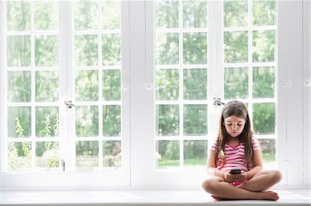 simsearch:6118-07781830,k - A girl sitting playing, holding a smart phone. Photographie de stock - Premium Libres de Droits, Code: 6118-07781850