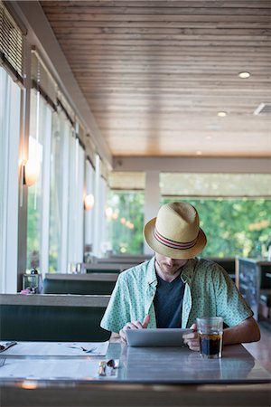 simsearch:6118-07781811,k - A man wearing a hat sitting in a diner using a digital tablet. Fotografie stock - Premium Royalty-Free, Codice: 6118-07781813