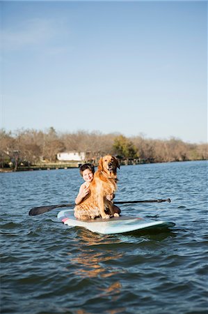 simsearch:6118-07731784,k - A child and a retriever dog sitting on a paddleboard on the water. Foto de stock - Sin royalties Premium, Código: 6118-07731794