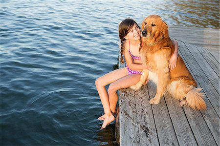 A girl and her golden retriever dog seated on a jetty by a lake. Foto de stock - Sin royalties Premium, Código: 6118-07731807