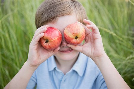 simsearch:6118-07732023,k - A boy holding two red skinned apples over his eyes. Photographie de stock - Premium Libres de Droits, Code: 6118-07731959