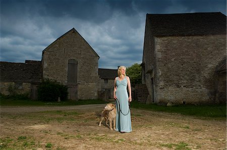 A woman with a lurcher dog in a farmyard, under a stormy sky. Photographie de stock - Premium Libres de Droits, Code: 6118-07731975