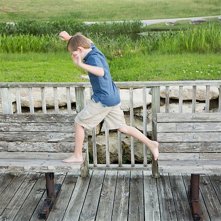 simsearch:6118-07732023,k - A young boy outdoors leaping from one bench to another on a jetty over water. Photographie de stock - Premium Libres de Droits, Code: 6118-07732045