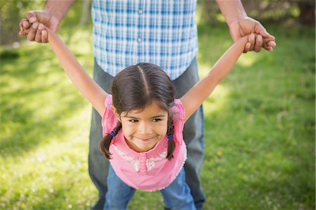 A young child in a pink dress with her arms outstretched playing with her father. Stock Photo - Premium Royalty-Free, Code: 6118-07732057