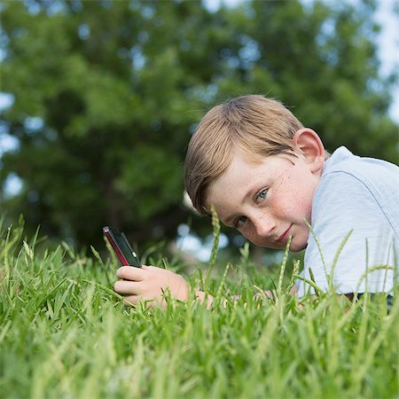 simsearch:6118-07732027,k - A young boy sitting on the grass using a hand held electronic games device. Stock Photo - Premium Royalty-Free, Code: 6118-07732010