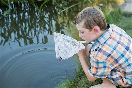 fishing kids - A young boy outdoors with a fishing net, examining the objects in the net, on a river bank. Stock Photo - Premium Royalty-Free, Code: 6118-07732023