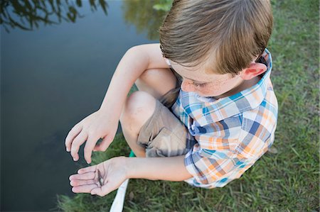 A young boy outdoors sitting on a riverbank with a small fish in the palm of his hand. Stockbilder - Premium RF Lizenzfrei, Bildnummer: 6118-07732021