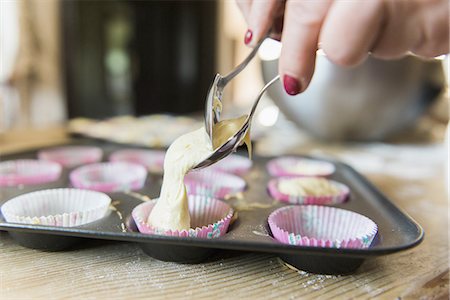 A woman at a kitchen table baking fairy cakes. Stock Photo - Premium Royalty-Free, Code: 6118-07808940