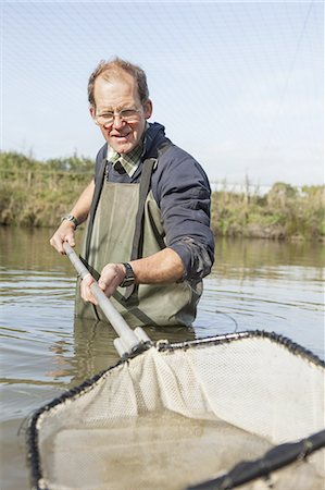 A man fishing carp, standing up to his waist in water with a large net. Fotografie stock - Premium Royalty-Free, Codice: 6118-07808984