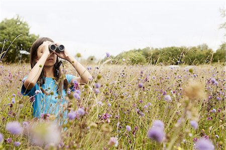 person looking at nature - A girl holding binoculars, a young bird watcher standing in a meadow of tall grass and wild flowers. Stock Photo - Premium Royalty-Free, Code: 6118-07808921