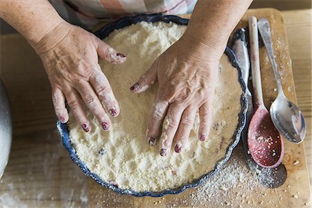 Woman patting crumble mixture into a pie dish, making a fruit crumble pudding. Foto de stock - Sin royalties Premium, Código: 6118-07808932