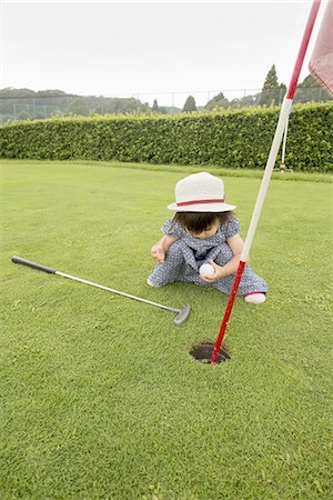 Young girl sitting by a golf course hole. Photographie de stock - Premium Libres de Droits, Code: 6118-07813245