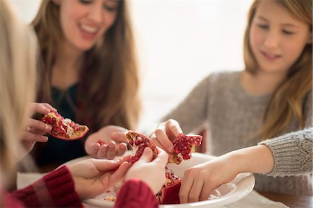 simsearch:6118-07769571,k - Two girls and a woman sitting at a table, picking kernels from a pomegranate. Fotografie stock - Premium Royalty-Free, Codice: 6118-07966879