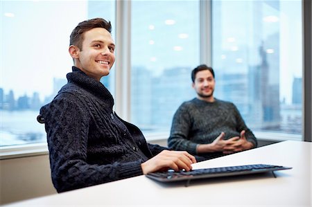 simsearch:6118-08066748,k - Two men in a office seated at a desk chatting and smiling. Stock Photo - Premium Royalty-Free, Code: 6118-08066743