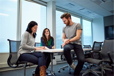 female sitting office chair - Three colleagues at a meeting, two women and a man seated on edge of the table. Looking over proofs of printed pages and designs. A creative environment. Stock Photo - Premium Royalty-Free, Code: 6118-08066746