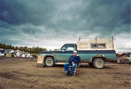 ferraille - A mature man seated in a chair by his pick up truck. Piles of waste, scrap metal and wood objects. Photographie de stock - Premium Libres de Droits, Code: 6118-08066770