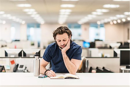 simsearch:622-08657638,k - A man leaning on  his elbow and looking at an open book on an office desk. Stock Photo - Premium Royalty-Free, Code: 6118-08066731