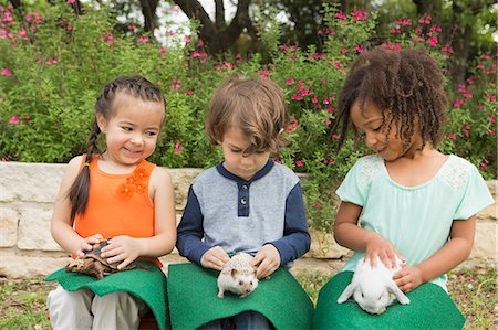Three children seated in a row, each with a small animal on their lap. Stock Photo - Premium Royalty-Free, Code: 6118-08081857