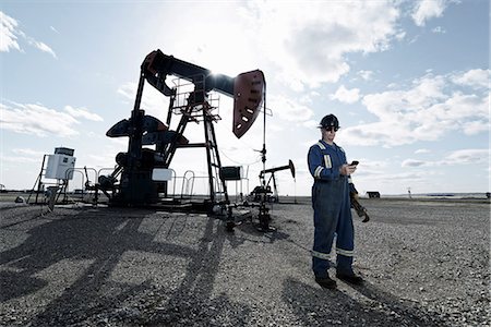 simsearch:6118-08088552,k - A man in overalls and hard hat at a pump jack in open ground at an oil extraction site. Stockbilder - Premium RF Lizenzfrei, Bildnummer: 6118-08081888