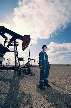 A man in overalls and hard hat at a pump jack in open ground at an oil extraction site. Foto de stock - Sin royalties Premium, Código: 6118-08081889