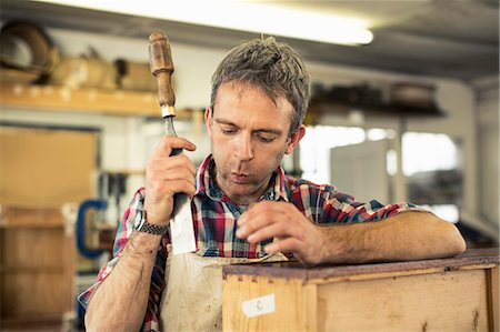 simsearch:6118-08725907,k - An antique furniture restorer holding a chisel and working on a polished wood surface, blowing away dust. Foto de stock - Royalty Free Premium, Número: 6118-08088592