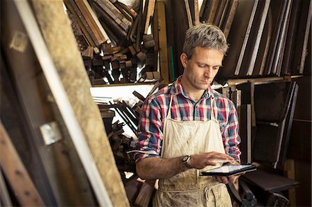 An antique furniture restorer in his workshop, using a digital tablet. Stockbilder - Premium RF Lizenzfrei, Bildnummer: 6118-08088596