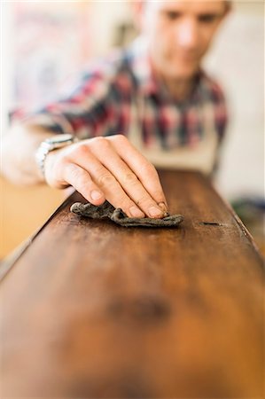simsearch:6118-08725907,k - An antique furniture restorer at work, using a cloth to polish a smooth wooden surface. Foto de stock - Royalty Free Premium, Número: 6118-08088604