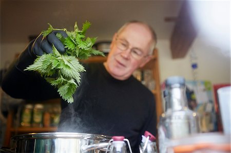 A man holding fresh foraged nettles with a gloved hand, blanching them in a pot. Stock Photo - Premium Royalty-Free, Code: 6118-08023754