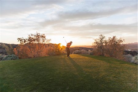 A man taking a shot off a golf tee on a golf course into the sunset. Stock Photo - Premium Royalty-Free, Code: 6118-08023761