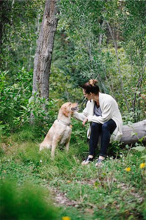 A woman seated on a log patting her retriever dog. Foto de stock - Royalty Free Premium, Número: 6118-08023715