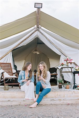 simsearch:6118-08140227,k - Two smiling women sitting outside a large tent laughing and having a glass of wine. Photographie de stock - Premium Libres de Droits, Code: 6118-08140151