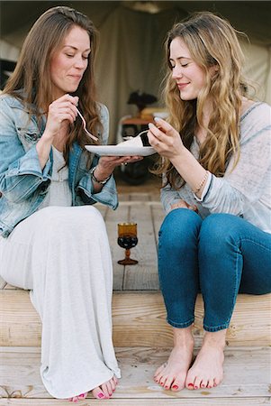 Two women sitting outdoors, sharing cake and a glass of wine. Stock Photo - Premium Royalty-Free, Code: 6118-08140154