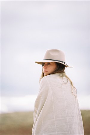 Woman wearing a hat and wrap looking over her shoulder, smiling at the camera. Stock Photo - Premium Royalty-Free, Code: 6118-08140199