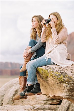 Two women sitting side by side on a rock in a desert, one taking a picture. Stock Photo - Premium Royalty-Free, Code: 6118-08140201