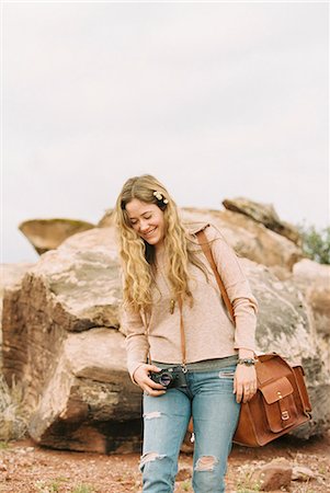 simsearch:6118-08140227,k - Smiling woman standing by a rock in a desert, carrying a leather bag. Photographie de stock - Premium Libres de Droits, Code: 6118-08140223