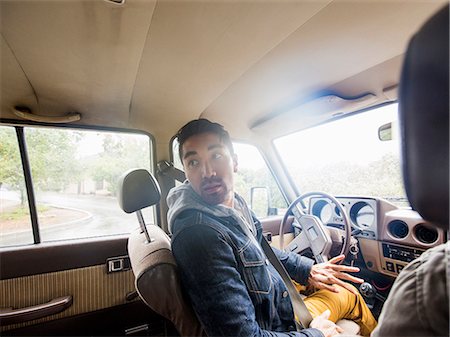 Young man in a car, in the driver seat, looking over his shoulder. Stock Photo - Premium Royalty-Free, Code: 6118-08129632