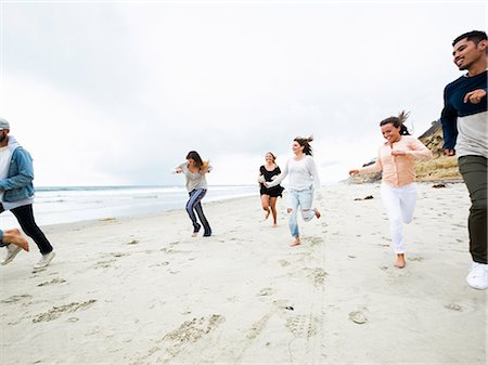 simsearch:6118-08129644,k - A group of young men and women running on a beach, having fun. Fotografie stock - Premium Royalty-Free, Codice: 6118-08129709