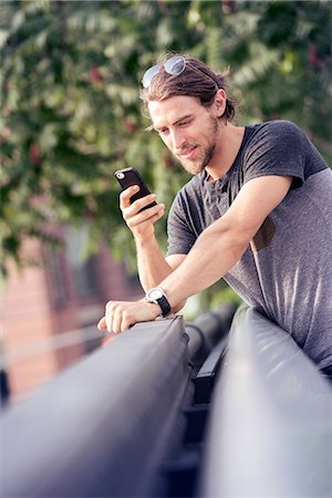 A young man leaning on a park railing checking his cell phone Stock Photo - Premium Royalty-Free, Code: 6118-08243833