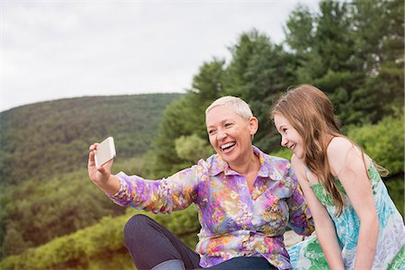 phone family selfie outside - A woman and a child seated on a lake dock taking a selfie with a smart phone. Stock Photo - Premium Royalty-Free, Code: 6118-08243931