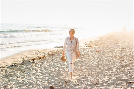 simsearch:6118-08140206,k - Woman walking along a sandy beach by the ocean. Foto de stock - Royalty Free Premium, Número: 6118-08282268