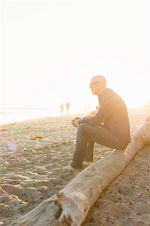 Bald man sitting on a log on a sandy beach. Stock Photo - Premium Royalty-Free, Code: 6118-08282270