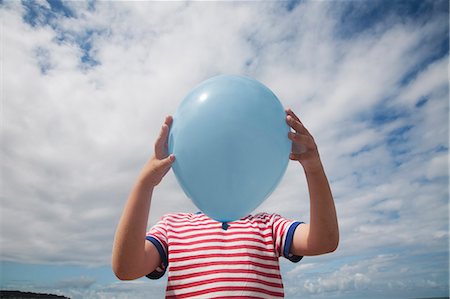 A boy standing holding a balloon in front of his face. Stock Photo - Premium Royalty-Free, Code: 6118-08282219