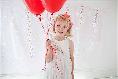 Young girl posing for a picture in a photographers studio, holding red balloons. Stock Photo - Premium Royalty-Free, Code: 6118-08282313