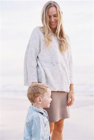 Smiling woman standing on a sandy beach by the ocean with her young son. Stock Photo - Premium Royalty-Free, Code: 6118-08202459
