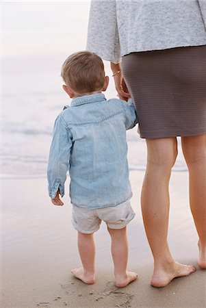 Woman standing on a sandy beach by the ocean, holding her young son's hand. Stock Photo - Premium Royalty-Free, Code: 6118-08202460
