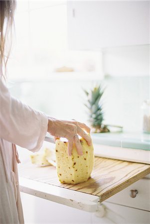 simsearch:6118-08023760,k - Woman standing in a kitchen, cutting a fresh pineapple. Stock Photo - Premium Royalty-Free, Code: 6118-08202481